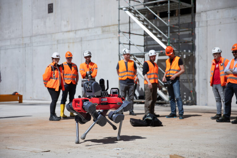 Metal industry workers observing an autonomous inspection robot at a steel plant site.